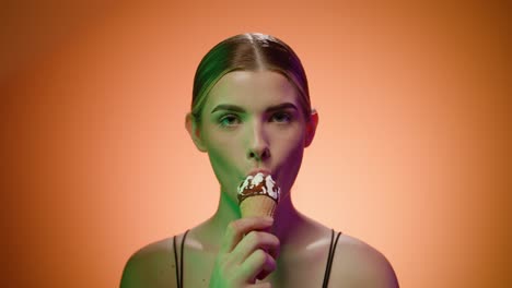 Cute-caucasian-woman-model-eats-a-ice-cream-cone,-studio-shot,-brown-background