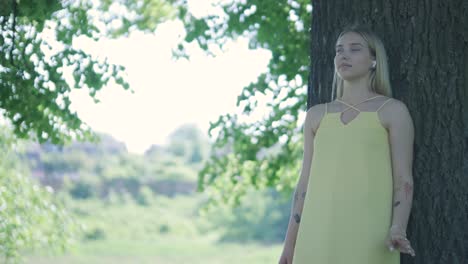 woman in yellow dress dancing by tree in summer park