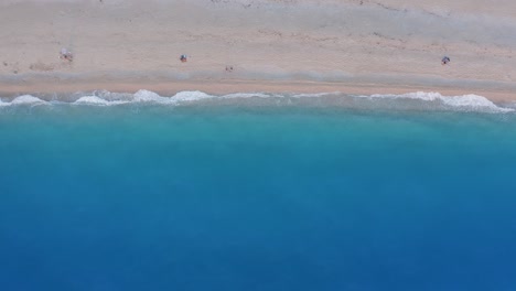 milos beach, lefkada, greece. top down view of golden sand and fluorescent, turquoise sea waves. unrecognizable people enjoying summer scene during sunset time