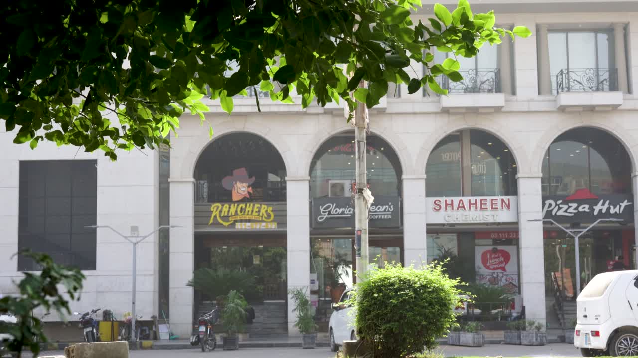 Street view of commercial buildings in Pakistan featuring Ranchers, Gloria Jean's, Shaheen Chemist, and Pizza Hut
