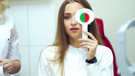 Young woman checking eyesight. Pretty girl doing vision test with one eye closed by occluder. Ophthalmology. Vision check-up.