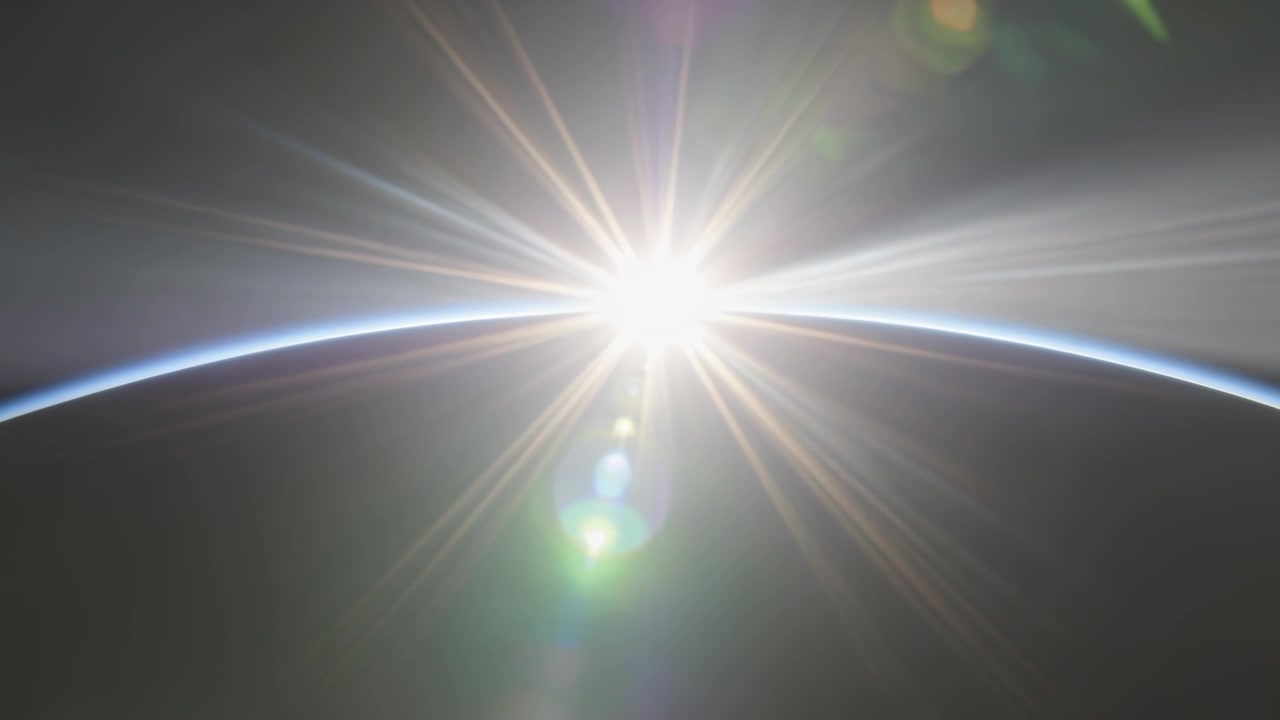 Mostrando un'esplosione solare mentre il sole sorge sopra il bordo della Terra da un'orbita bassa, creando bagliori verdi dell'obiettivo.