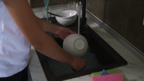 Close-Up-view-of-female-hands-washing-dishes-in-modern-kitchen.-Slow-Motion-shot