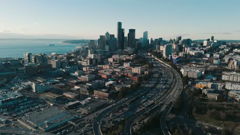 high drone flyover of afternoon traffic with long shadows, seattle skyline, and puget sound backdrop