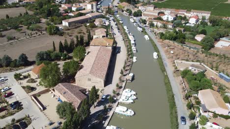 le-Somail-Canal-du-Midi-France,-drone-view-of-the-canal-and-village,-boats-tied-up-and-romantic-bridge