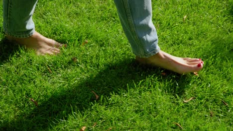 Nahaufnahme-Einer-Frau,-Die-Barfuß-In-Jeans-Durch-Einen-Grünen,-üppigen-Rasen-Geht-Und-Einen-Schatten-In-Richtung-Der-Kamera-Wirft