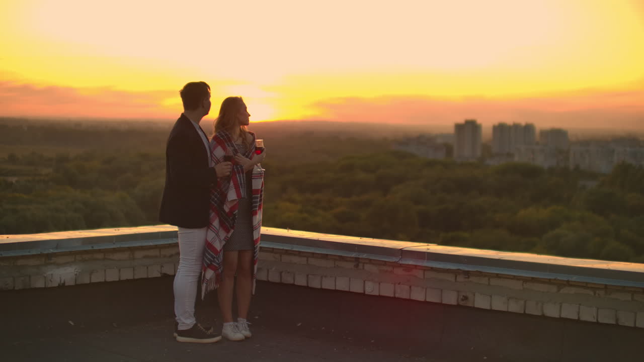 Amanti che si abbracciano, un ragazzo e una ragazza che guardano il tramonto con del vino in piedi sul tetto dell'edificio. Video al rallentatore della relazione di una giovane coppia sposata.