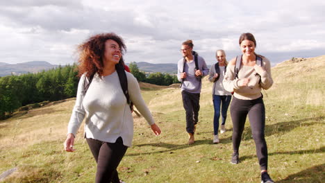 A-multi-ethnic-group-of-five-happy-young-adult-friends-walking-across-a-field-during-a-mountain-hike,-close-up