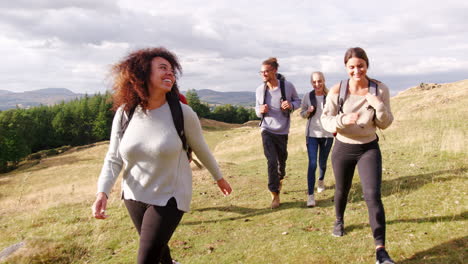 a multi ethnic group of five happy young adult friends walking across a field during a mountain hike, close up