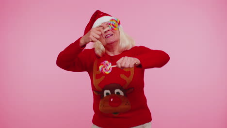 senior grandmother in christmas sweater holding candy striped lollipops, dancing making silly faces