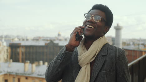 African-American-Businessman-Walking-on-Rooftop-Terrace-and-Speaking-on-Phone