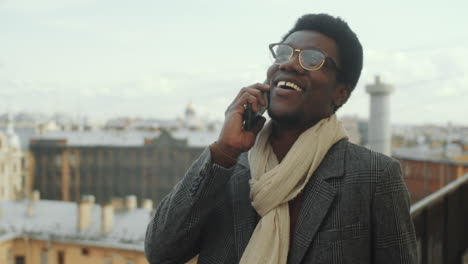 african american businessman walking on rooftop terrace and speaking on phone