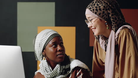 female muslim colleagues talking by desk