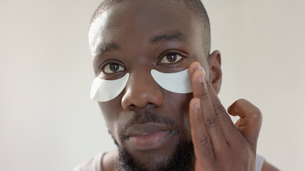 Applying under-eye patches, African American man enjoying skincare routine at home spa