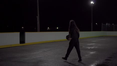 teenage girl with brown hair and black sweater shoots basketball in at outdoor court in the dark with lights