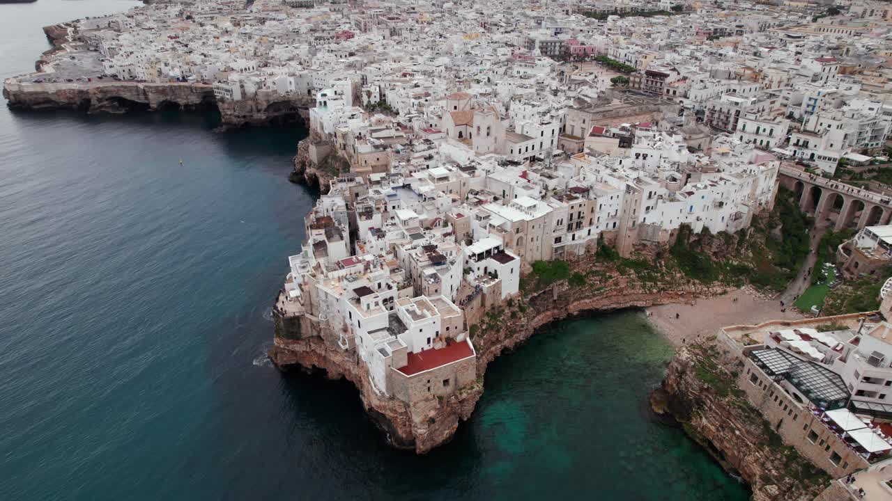 Aerial rising panorama of Polignano city on rocky cliff edge on adriatic sea coast