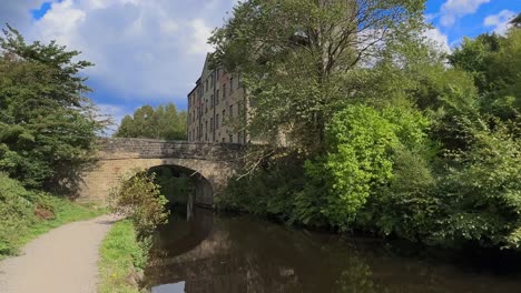 rustic scene set on a riverbank, canal side, showing a stone bridge and a old woolen mill