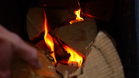 Hand,-Die-Geschnittene-Holzstämme-Ins-Feuer-Legt