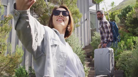 pareja feliz diversa con equipaje tomando selfie wirh teléfono inteligente en el jardín