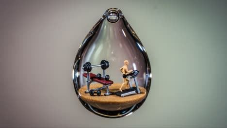a unique art installation: a miniature gym scene encased in a glass teardrop, showcasing the intricacies of fitness and wellbeing