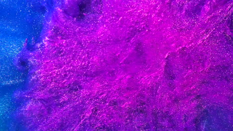 explosión de salpicaduras de tinta azul y rosa de colores abstractos en agua líquida con partículas metálicas que fluyen en cámara lenta