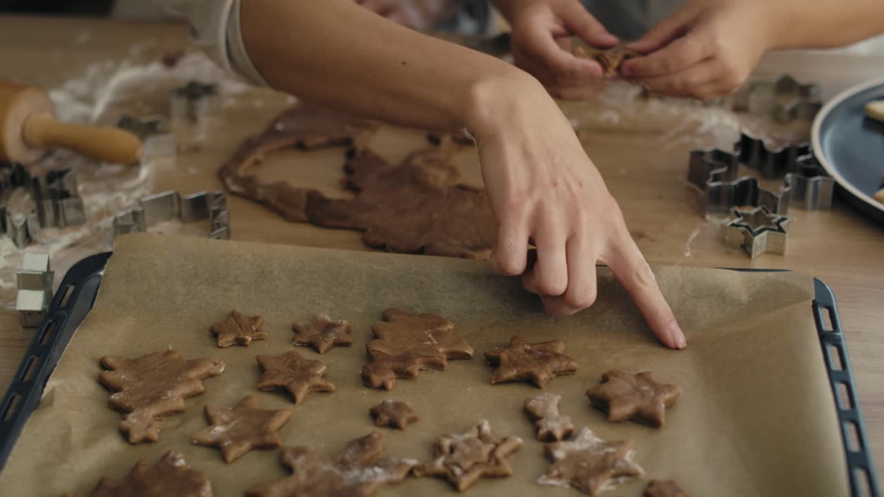 mujer irreconocible con su hija haciendo galletas de pan de jengibre con masa y poniéndolas en la bandeja de horneado.