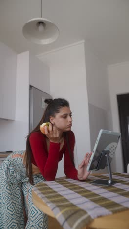 woman eating apple while using tablet in kitchen