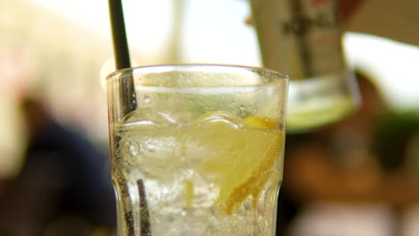 pouring carbonated water from a bottle into a transparent glass with ice, lemon, and a black paper straw