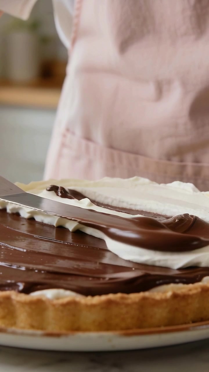 Video verticale: Cuoco con grembiule rosa che leviga dopo aver decorato con la sac à poche, finendo una crostata a casa con una spatola.