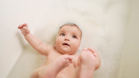 little baby girl lying on her back in the bathroom all in foam