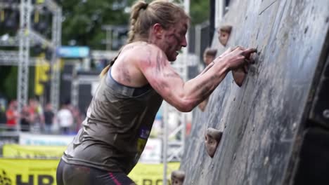 woman climbing muddy obstacle course wall