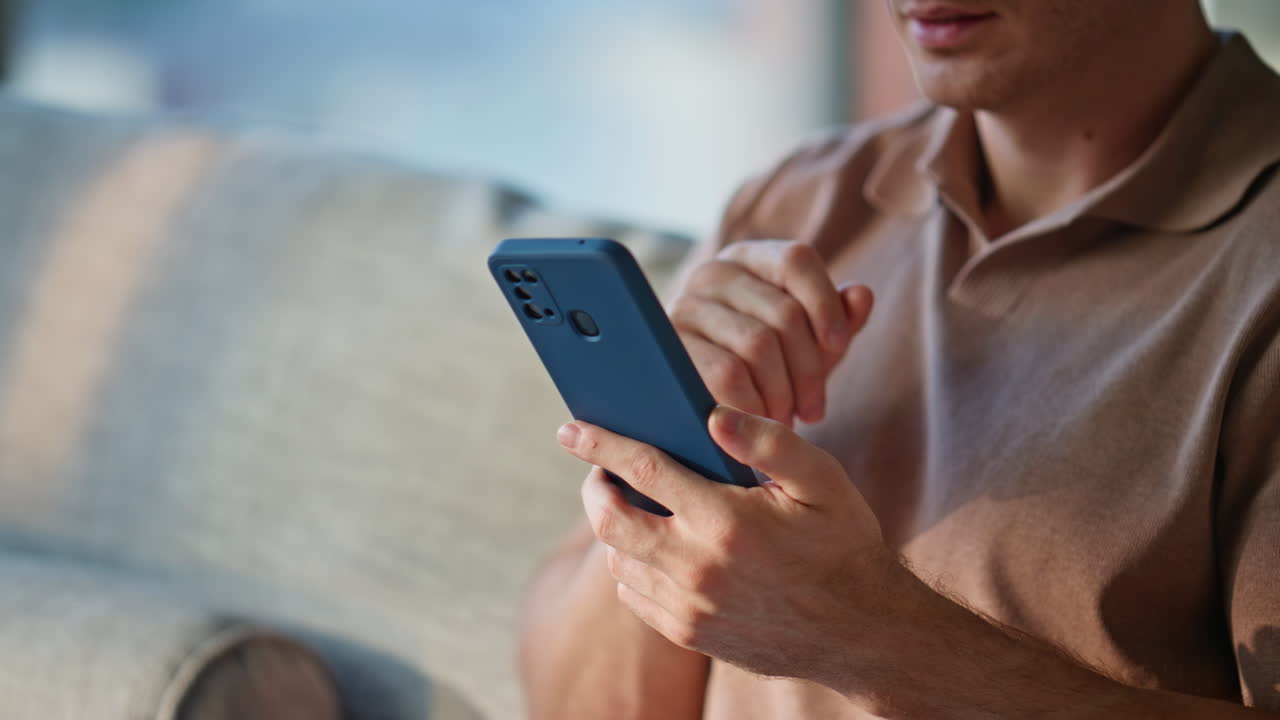 Cheerful guy looking smartphone on sofa modern apartment closeup. Smiling man