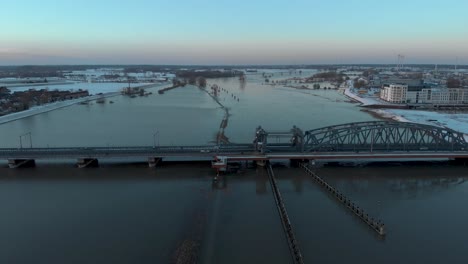 Sunset-aerial-backwards-movement-revealing-the-cityscape-of-Dutch-Hanseatic-medieval-tower-town-Zutphen-in-The-Netherlands-with-snow-on-the-boulevard-with-draw-bridge-over-river-IJssel-in-foreground