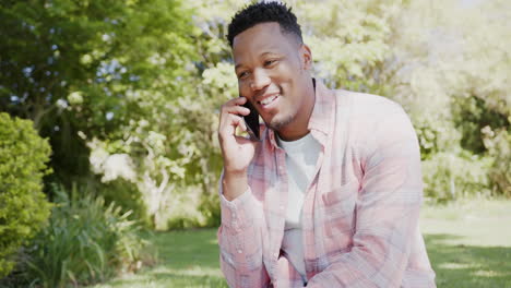 happy african american man talking on smartphone in garden at home, slow motion