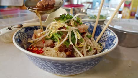 Pouring-Pork-Soup-Broth-Over-a-Bowl-of-Asian-Noodles-and-Toppings-in-Slow-Motion