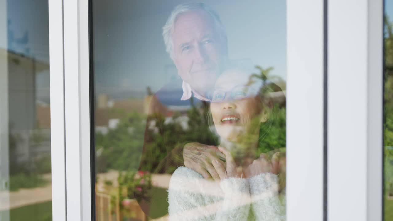 Happy diverse senior couple embracing and looking through window together