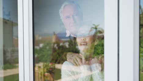 Happy-diverse-senior-couple-embracing-and-looking-through-window-together