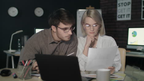 Business-couple-watching-together-financial-report-front-computer-in-dark-office