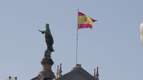 spanish flag waving next to a statue under clear blue skies in barcelona