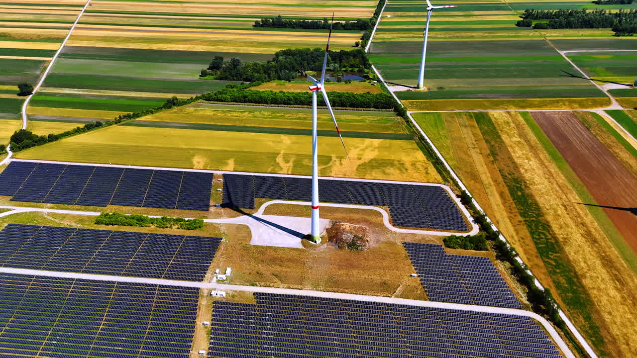 Several fields are covered by modern solar panels accumulating sunlight. Few wind turbines rotate in the wind