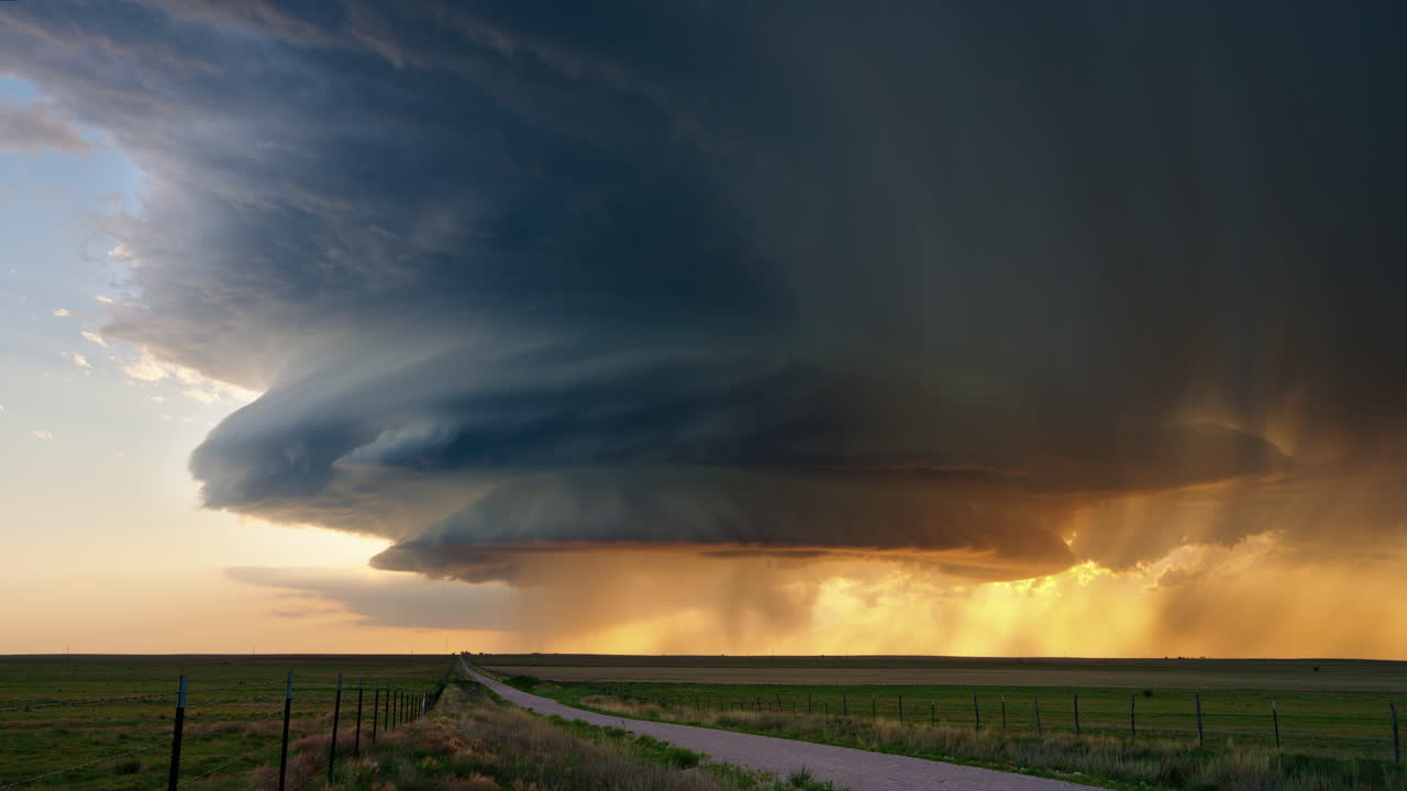 A dramatic supercell storm cloud over a vast prairie landscape at sunset or sunrise