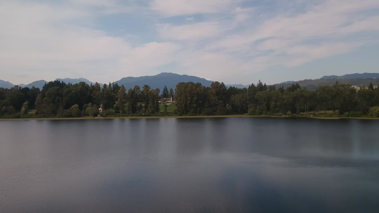 elevación aérea dolly rodar sobre el estanque del lago tranquilo alrededor de un exuberante bosque verde montaña del valle con reflejos tranquilos en el agua y el follaje ambiente pacífico abeto pino arce robles