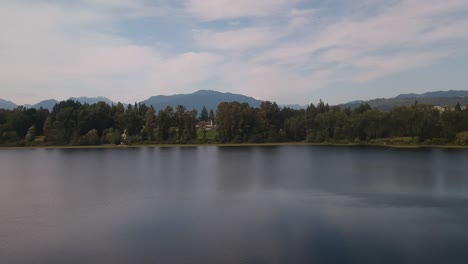 aerial rise dolly roll over calm lake pond around a lush green forest valley mountain with tranquil reflections on the water and the foliage peaceful environment fir pine maple oak trees