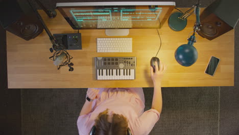 overhead view of female musician at workstation with keyboard and microphone in studio at night