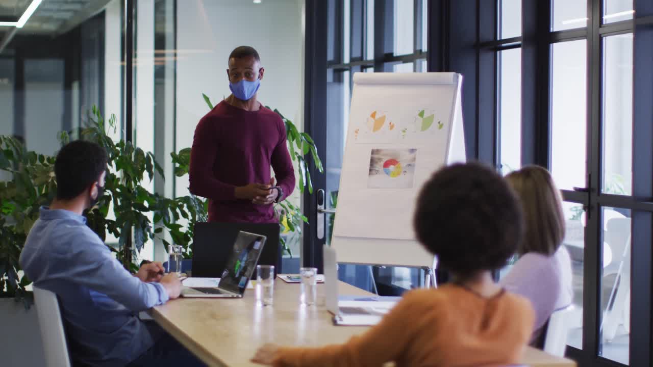 Diverse business people wearing masks sitting listening to a presentation in office