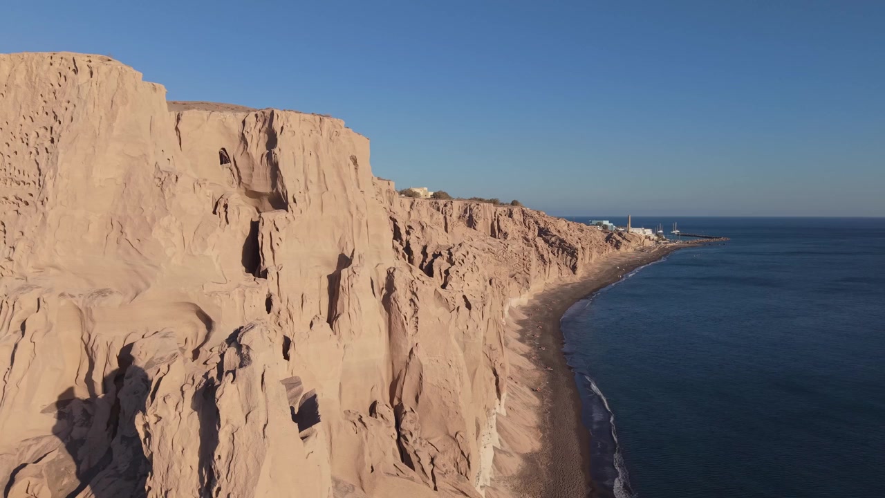 Droneoptagelser, der afslører den barske klippekystlinje ved Vlychada Strand på Santorini, og viser dramatiske vulkanske formationer samt det unikke kystlandskab.