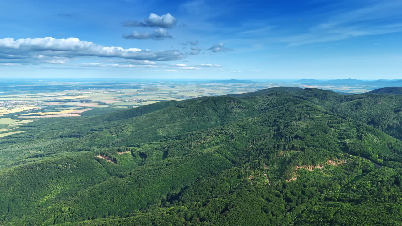Panoramic aerial view of mountains and green forest. A panoramic aerial view of green mountains and forests with valleys and open fields. Scenic landscape under a clear blue sky