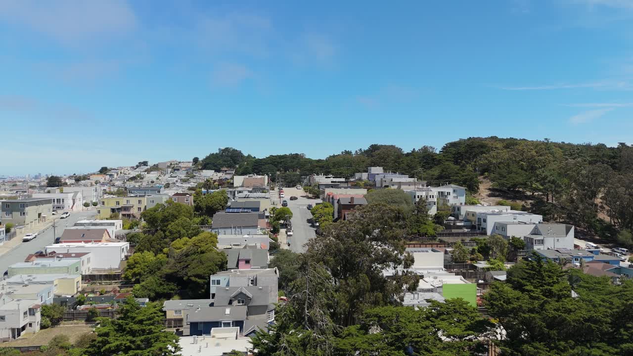 Descending Drone view showcases the Excelsior area of San Francisco, highlighting colorful houses, tree-lined blocks, and the rolling hills that create a dynamic and lively urban landscape