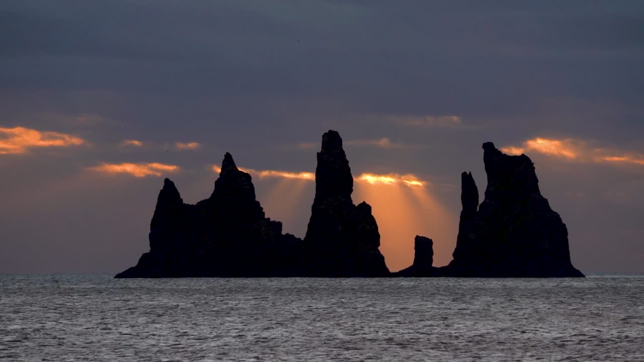 Faraglioni basaltici di Reynisdrangar in controluce con raggi di sole attraverso il cielo nuvoloso al tramonto in Islanda. Timelapse