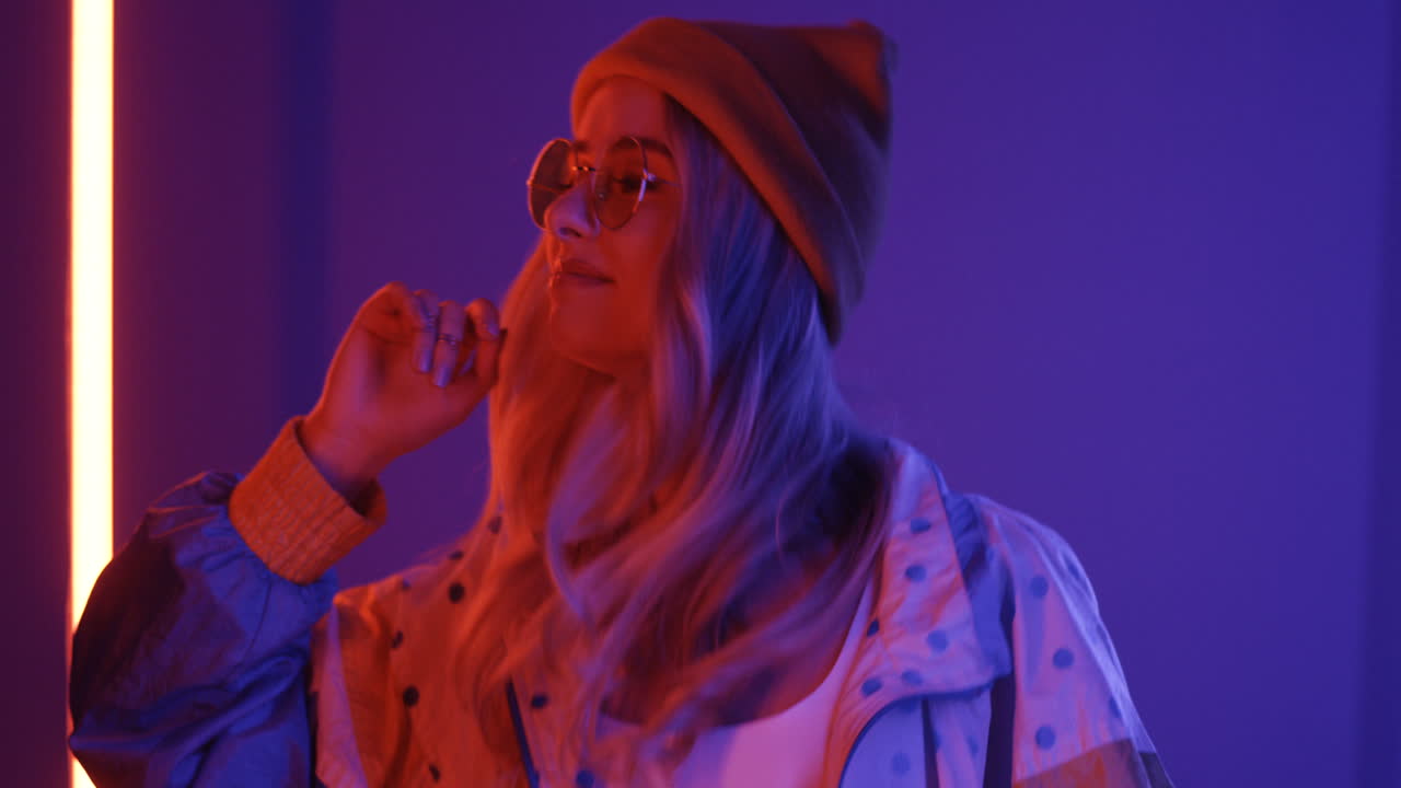 крупный план молодой светловолосой стильной девушки, смотрящей в камеру на фоне розового и фиолетового неонового света